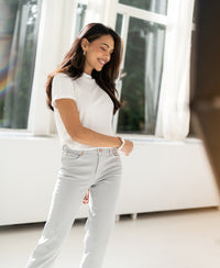 Woman wearing an ivory ribbed top by PLEIN PUBLIQUE standing indoors by sunlit windows.