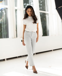 Woman wearing ivory ribbed collared top by PLEIN PUBLIQUE stands in a bright room, looking down.