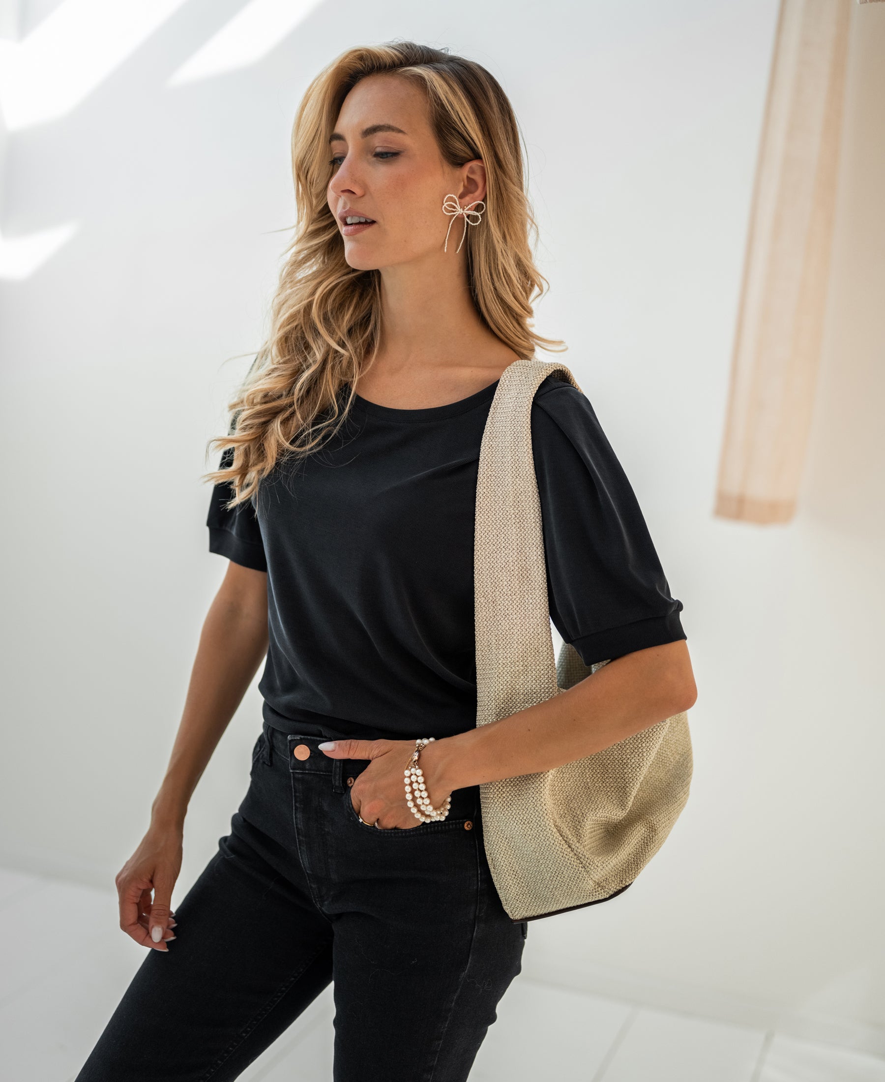 Charcoal ribbed T-shirt made of cotton, shown worn by a woman with long blonde hair in a bright room.
