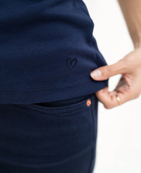 A hand lifts the hem of the Luxe & soft dark blue top by PLEIN PUBLIQUE, showing its fabric and texture.