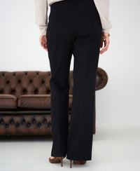 Woman stands before a brown leather sofa, wearing black flared pants.