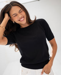 Woman wearing black sweater poses in bright light, hand in her hair.