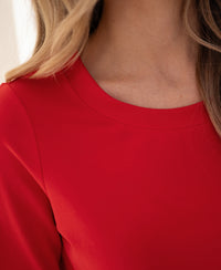 Close-up of a person wearing a PLEIN PUBLIQUE stretch short-sleeve T-shirt in coral red, showing the neckline and shoulder.