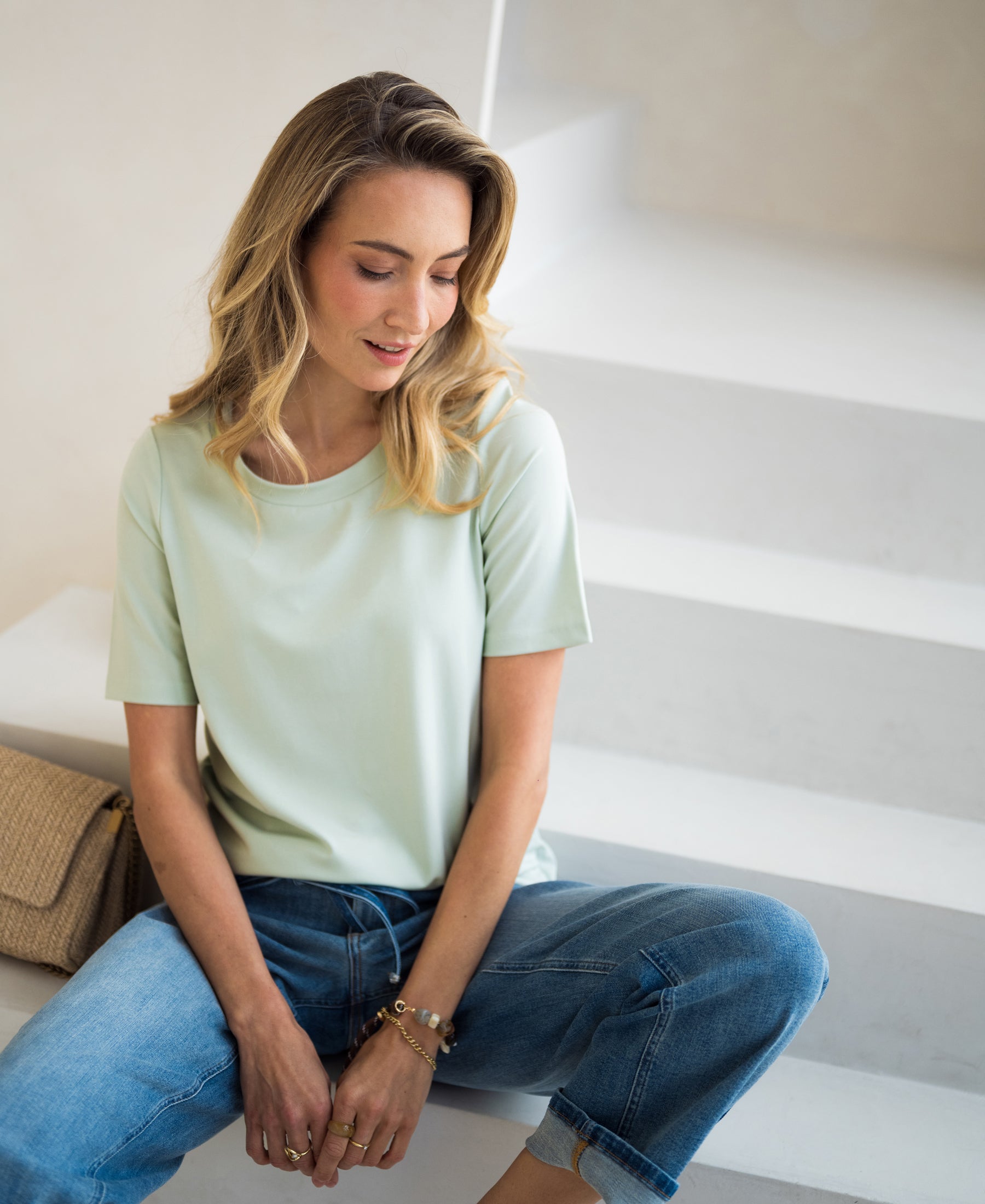 Stretch T-shirt with short sleeves in soft green by PLEIN PUBLIQUE, shown on a model on white stairs.