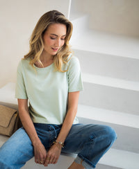 Stretch T-shirt with short sleeves in soft green by PLEIN PUBLIQUE, shown on a model on white stairs.