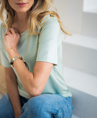 Woman wearing a light green stretch short-sleeve T-shirt by PLEIN PUBLIQUE.