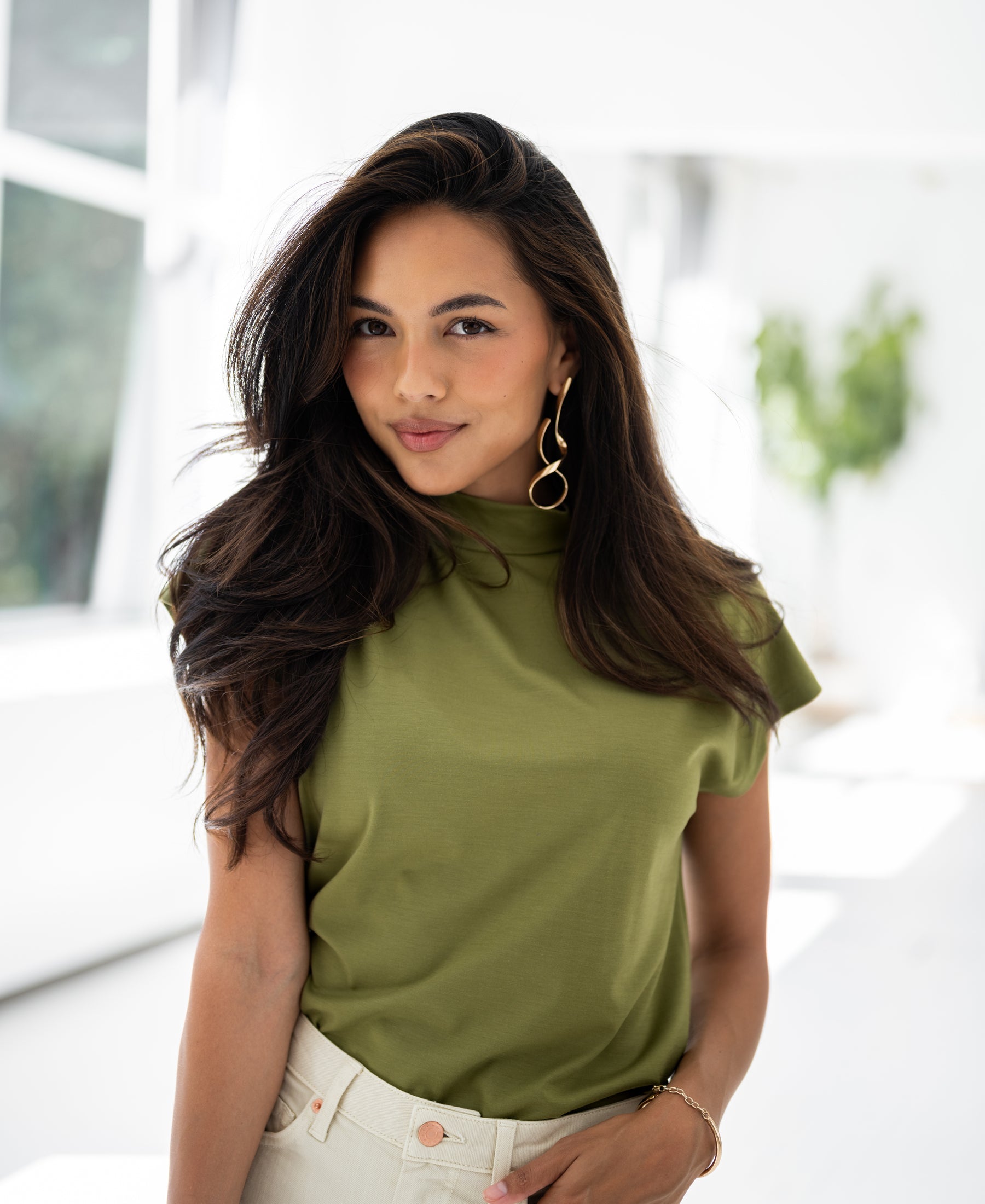 Woman wearing an olive green Plein Publique travel collared top, indoors.
