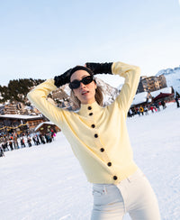 Soft yellow merino wool turtleneck vest by PLEIN PUBLIQUE shown against a snowy mountain background.
