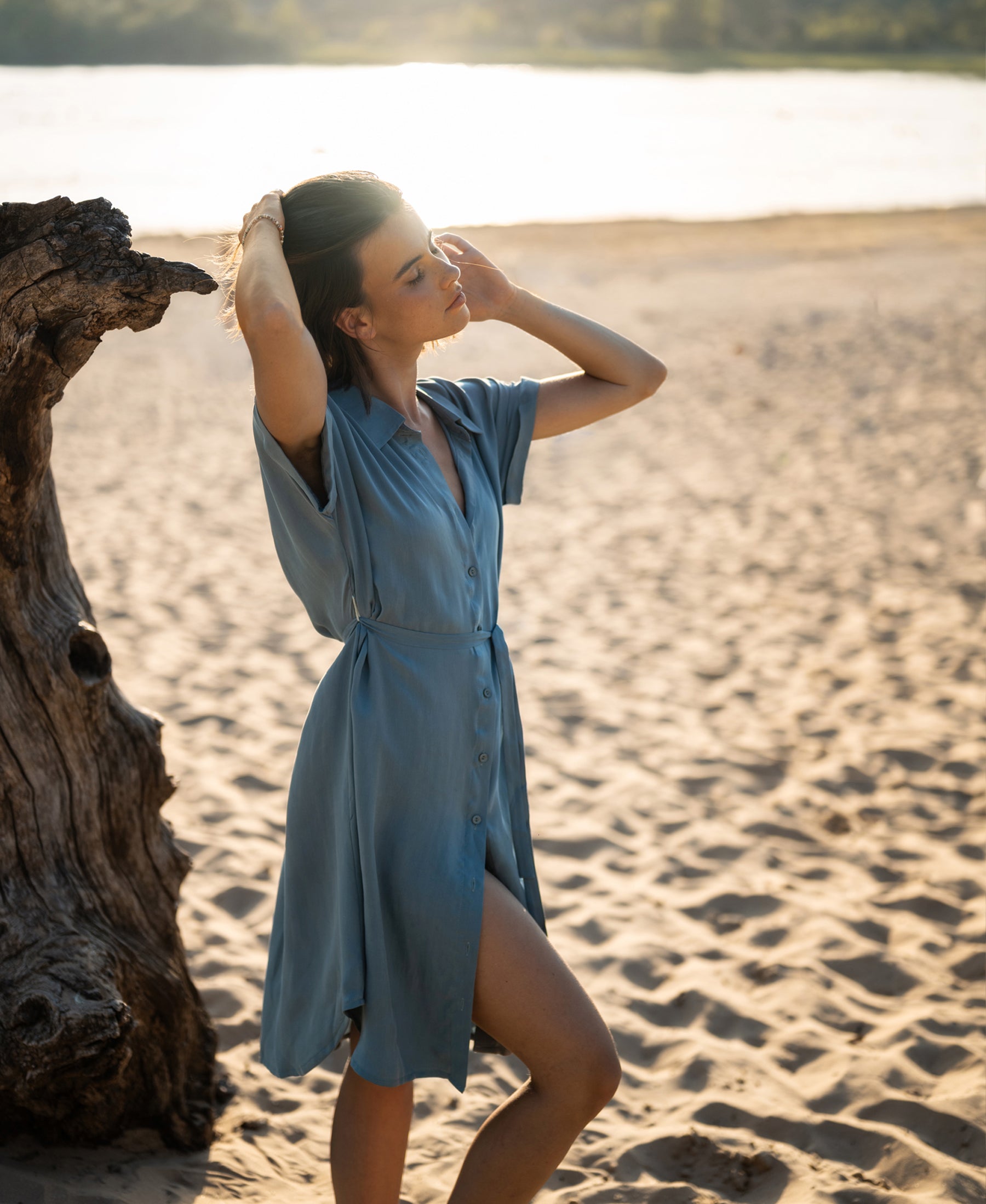 Cupro LA SELENE dress in Denim Cloud by Plein Publique shown outdoors with sunlight glowing behind.