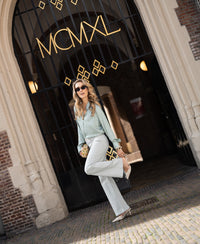 Woman wearing a light green and ivory polka dot blouse stands in front of an arched gate with gold MCMXL letters.