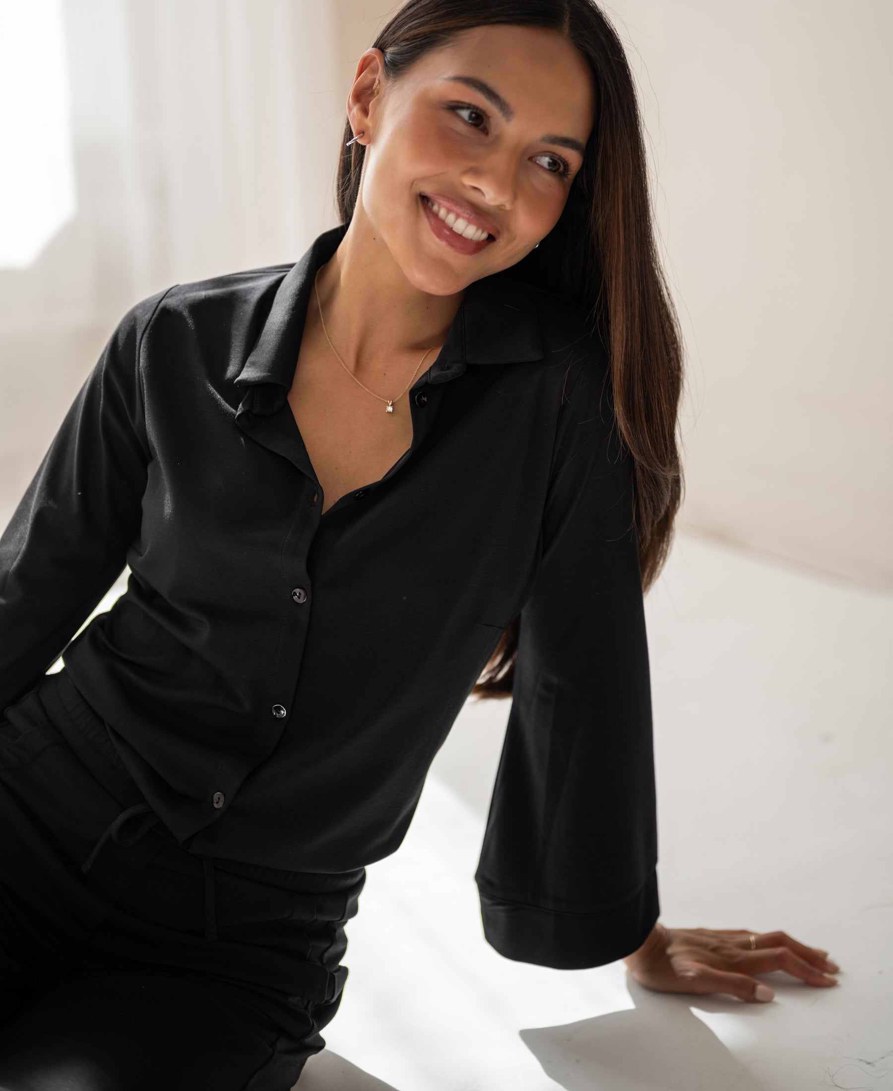 Woman with long dark hair wears the PLEIN PUBLIQUE black LA SILVESE travel blouse.