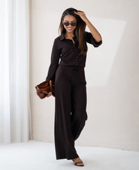 Woman wearing a chocolate brown travel blouse in a bright, minimalist room.