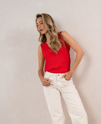 Woman wears a PLEIN PUBLIQUE Lyocell coral-colored top, posing against a light wall and looking down.