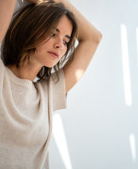 Light sand linen summer sweater, front view in natural light, model with arms raised.