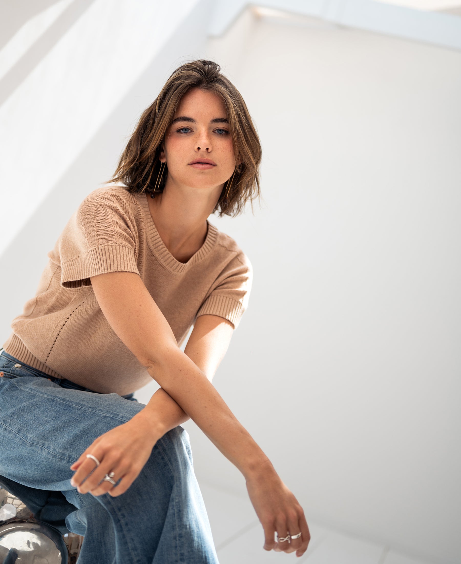 Woman wearing the LE SOLEIL Summer Sweater with linen in Soft Camel, seated indoors in natural light.