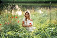 Woman wearing an ivory ribbed boat neck T-shirt sits by red flowers near a pond, looking thoughtful.