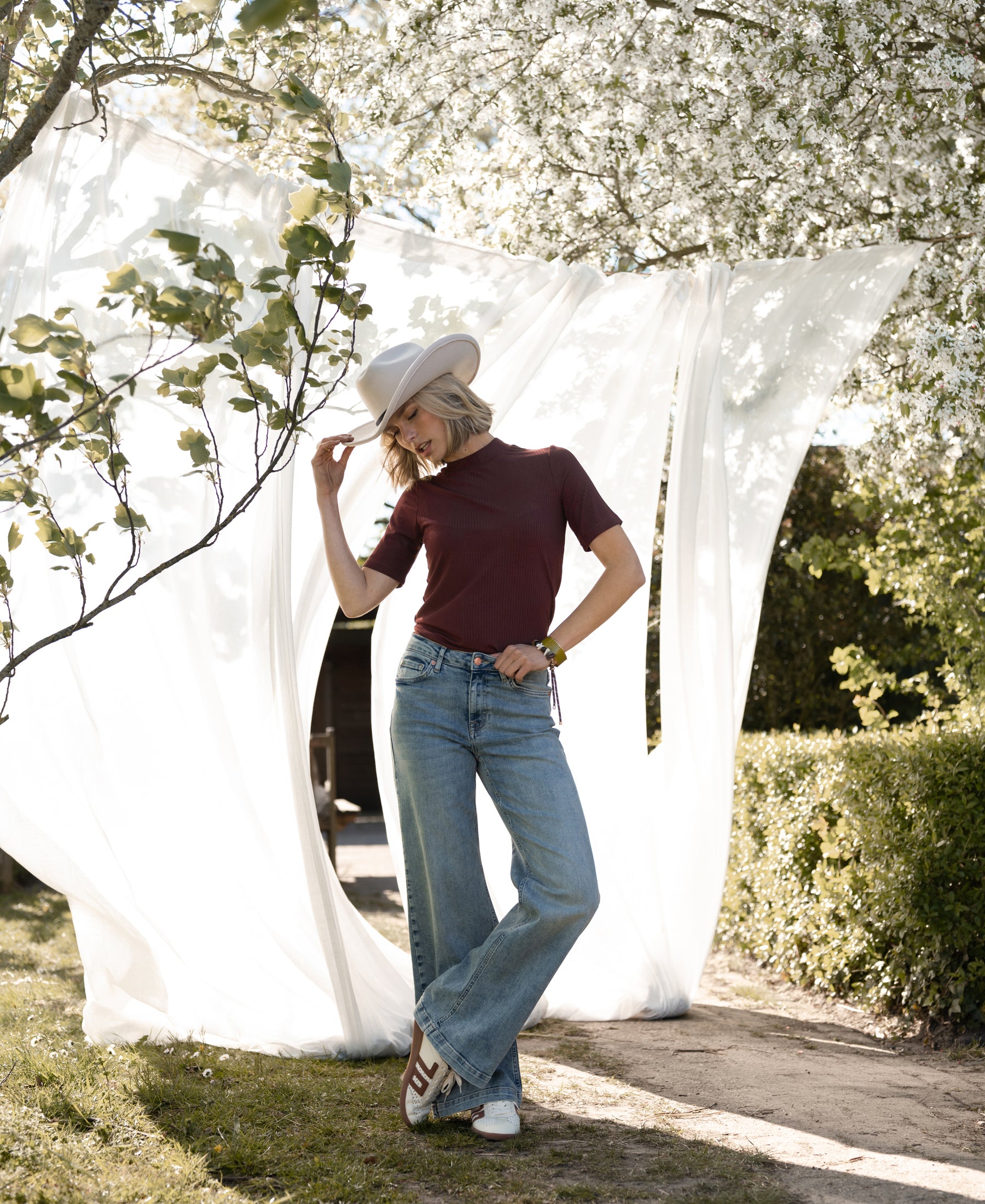 Woman wearing chestnut bamboo turtleneck top outdoors near fabric and blooming trees.