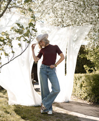 Woman wearing chestnut bamboo turtleneck top outdoors near fabric and blooming trees.