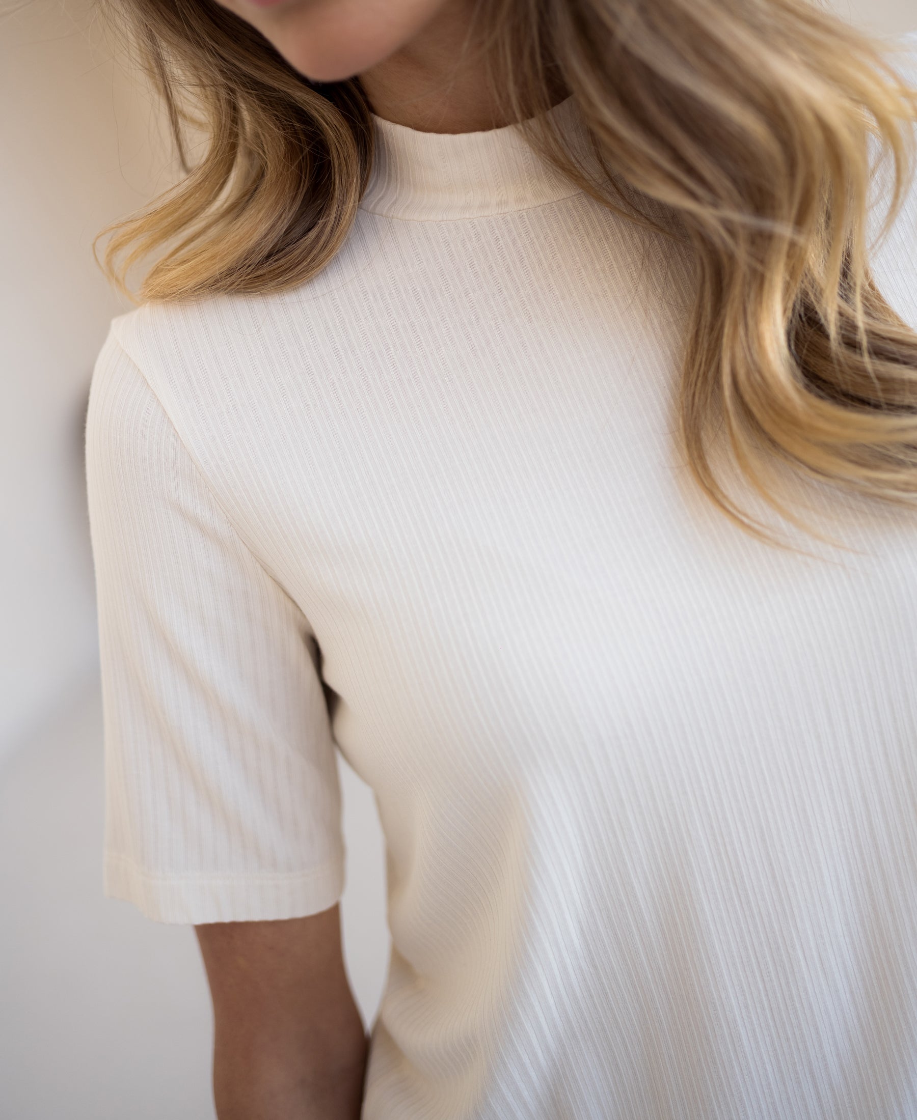 Cream bamboo turtleneck top shown from the shoulders down.