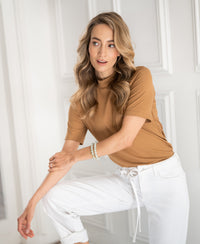 Woman wearing a gold-yellow bamboo turtleneck top by paneled walls.