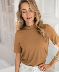 Woman wearing a gold-yellow bamboo turtleneck top, standing indoors.
