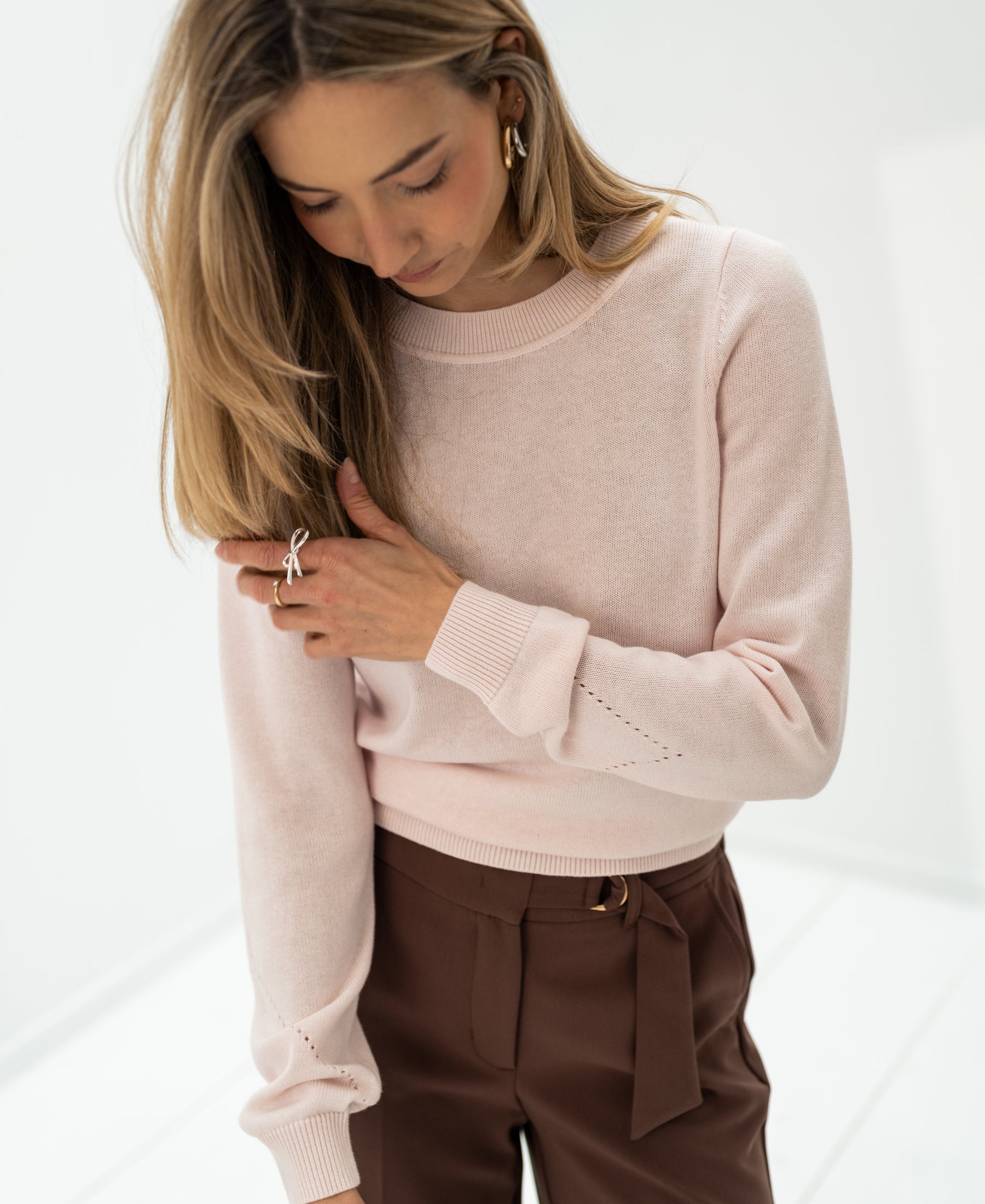 Woman wears blush Merino blend sweater in a bright, minimal space.