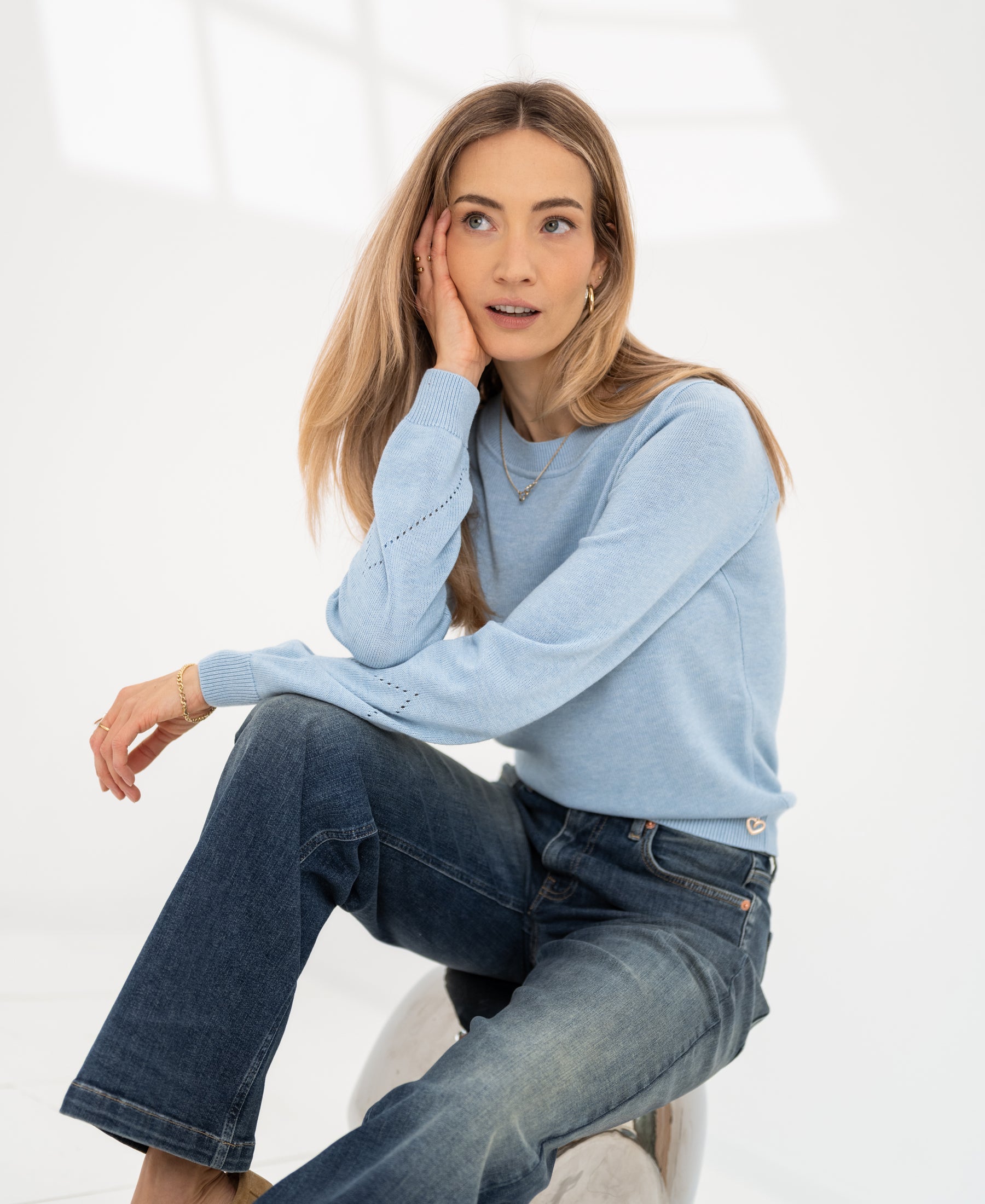 Light blue Merino wool blend sweater in bright light. Model’s hand partially covering face.