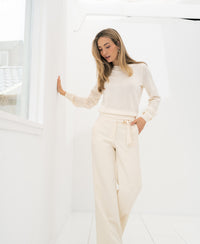 Woman wears the Merino blend sweater LE SONGE Ivory by PLEIN PUBLIQUE near a window in a bright room.