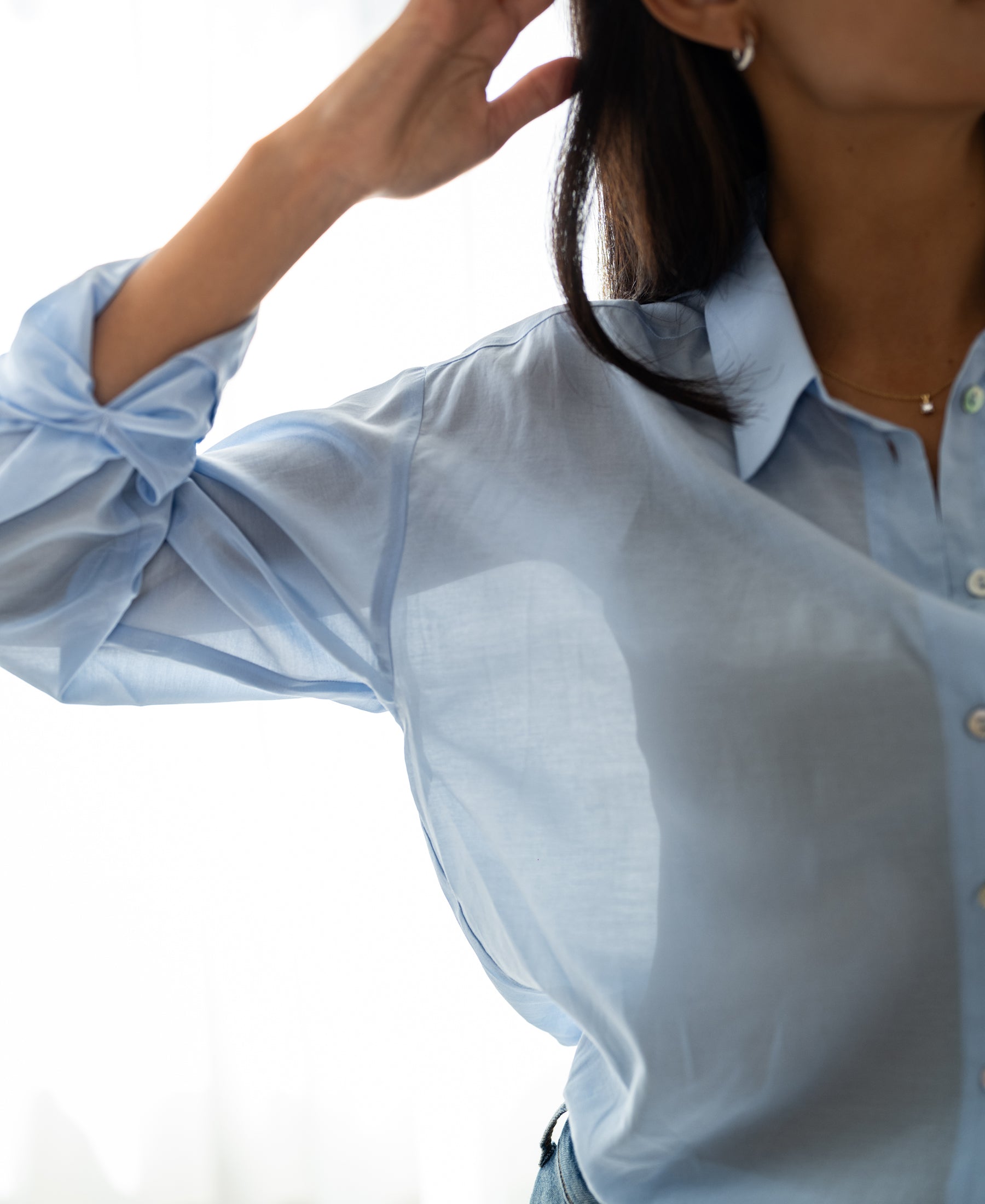 Light blue Dunne oversized blouse in silk, shown on a woman with one arm raised.