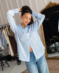 Dunne oversized blouse in light blue silk by PLEIN PUBLIQUE, shown worn in a chic indoor setting.