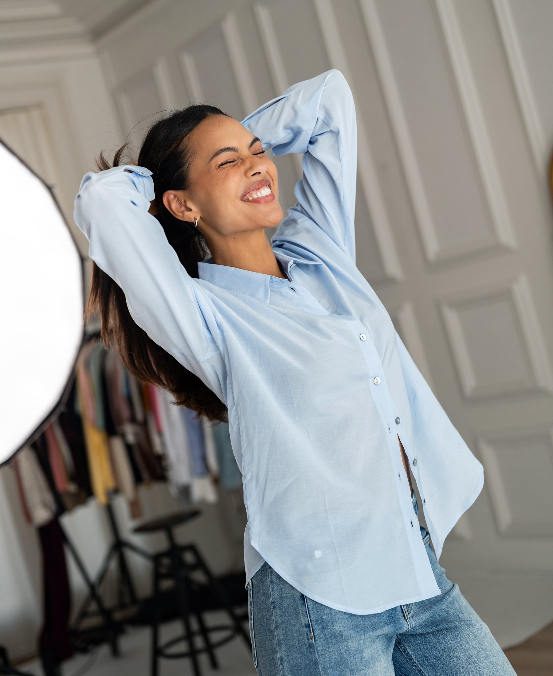 Oversized light blue blouse in silky fabric, shown on a model with arms raised.