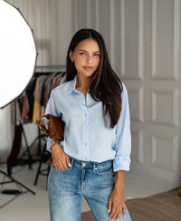 Woman wearing light blue silk oversized blouse indoors.