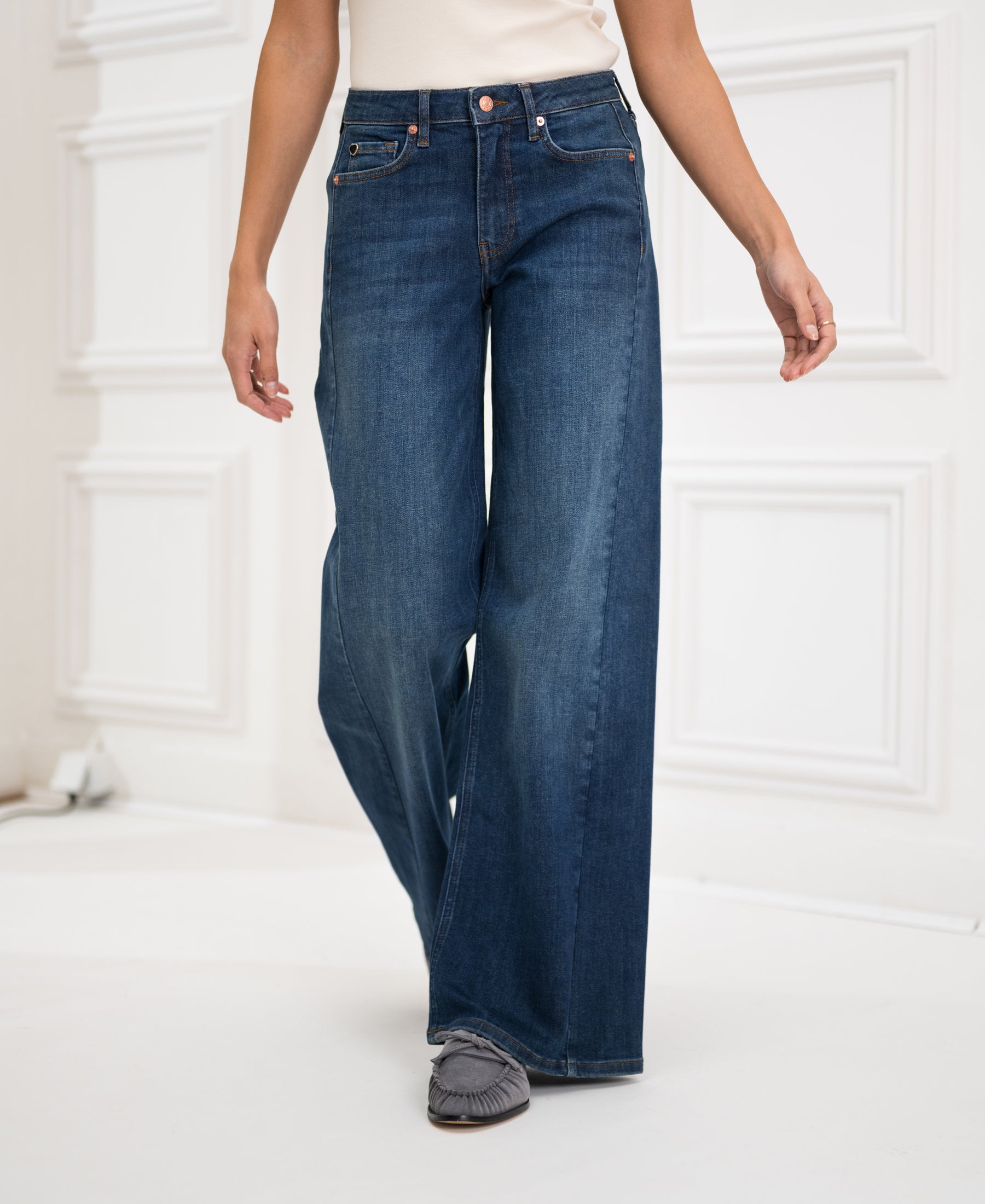 Wide leg blue heritage jeans in a relaxed fit, shown worn by a person standing by a white paneled wall.