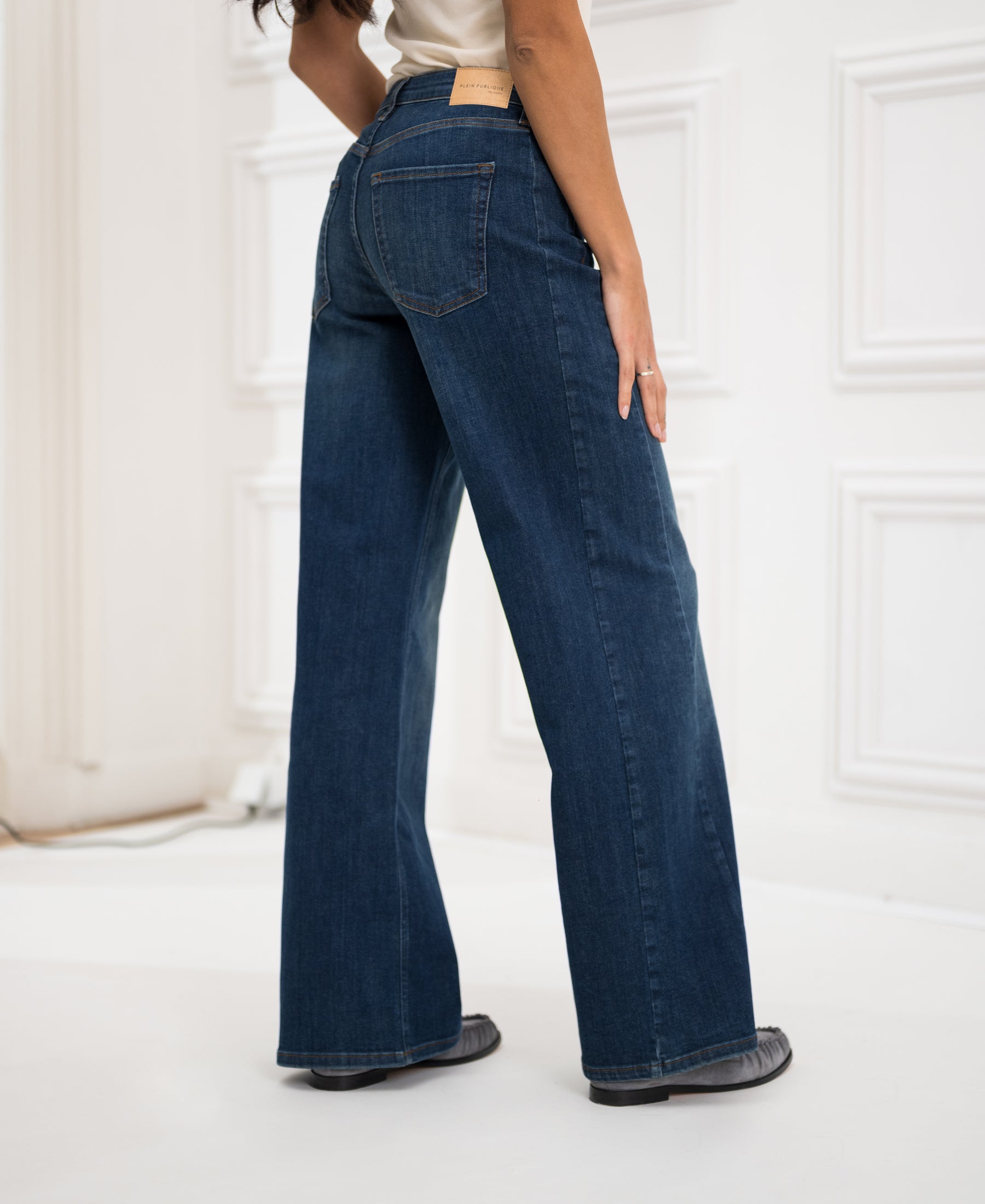 Person wearing relaxed fit blue heritage wide leg jeans, back view in a bright room.