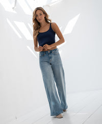 Woman wears navy silk cami top in a bright, sunlit white room.