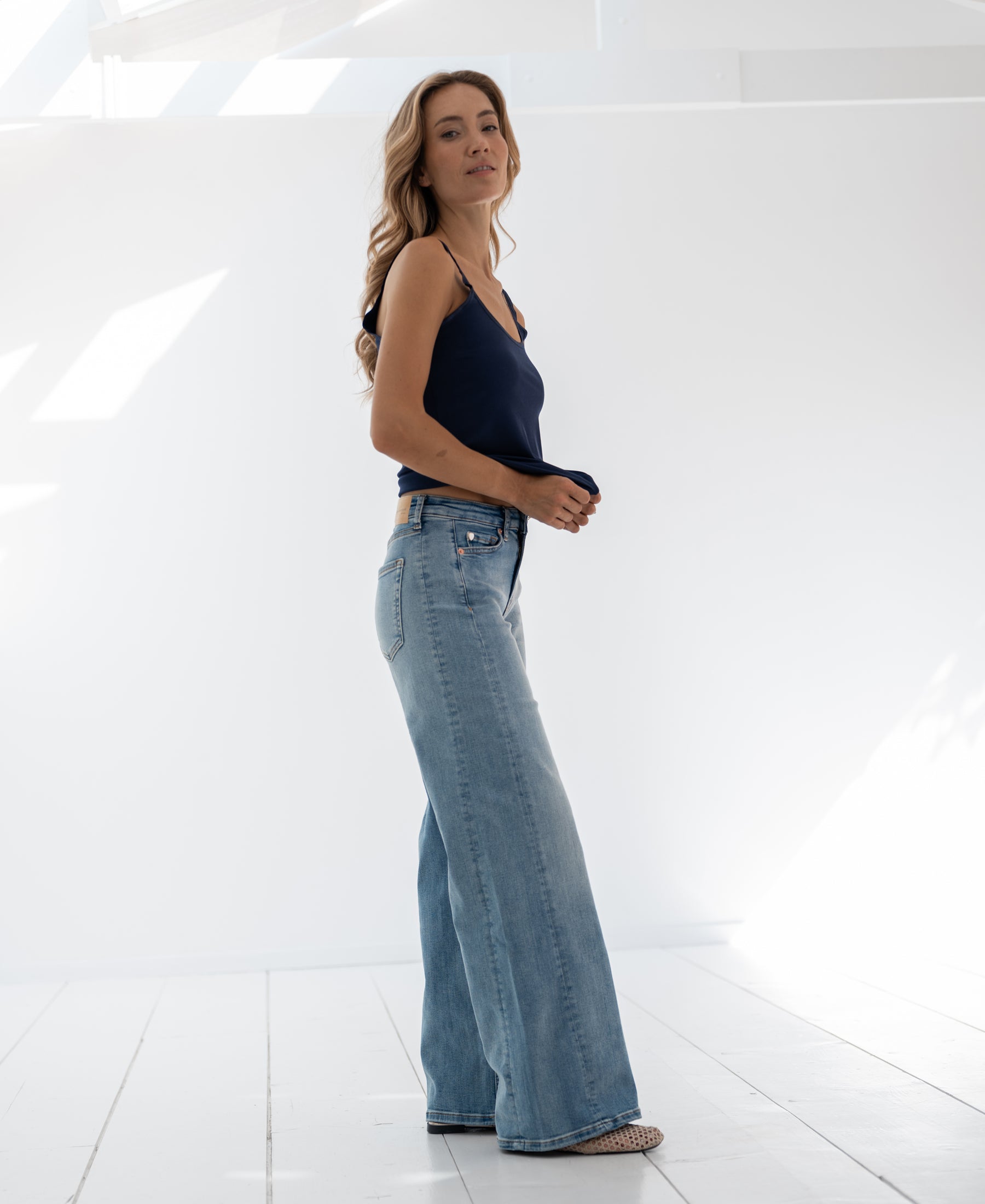 Light stone wide leg jeans displayed on white floor in sunlit room.