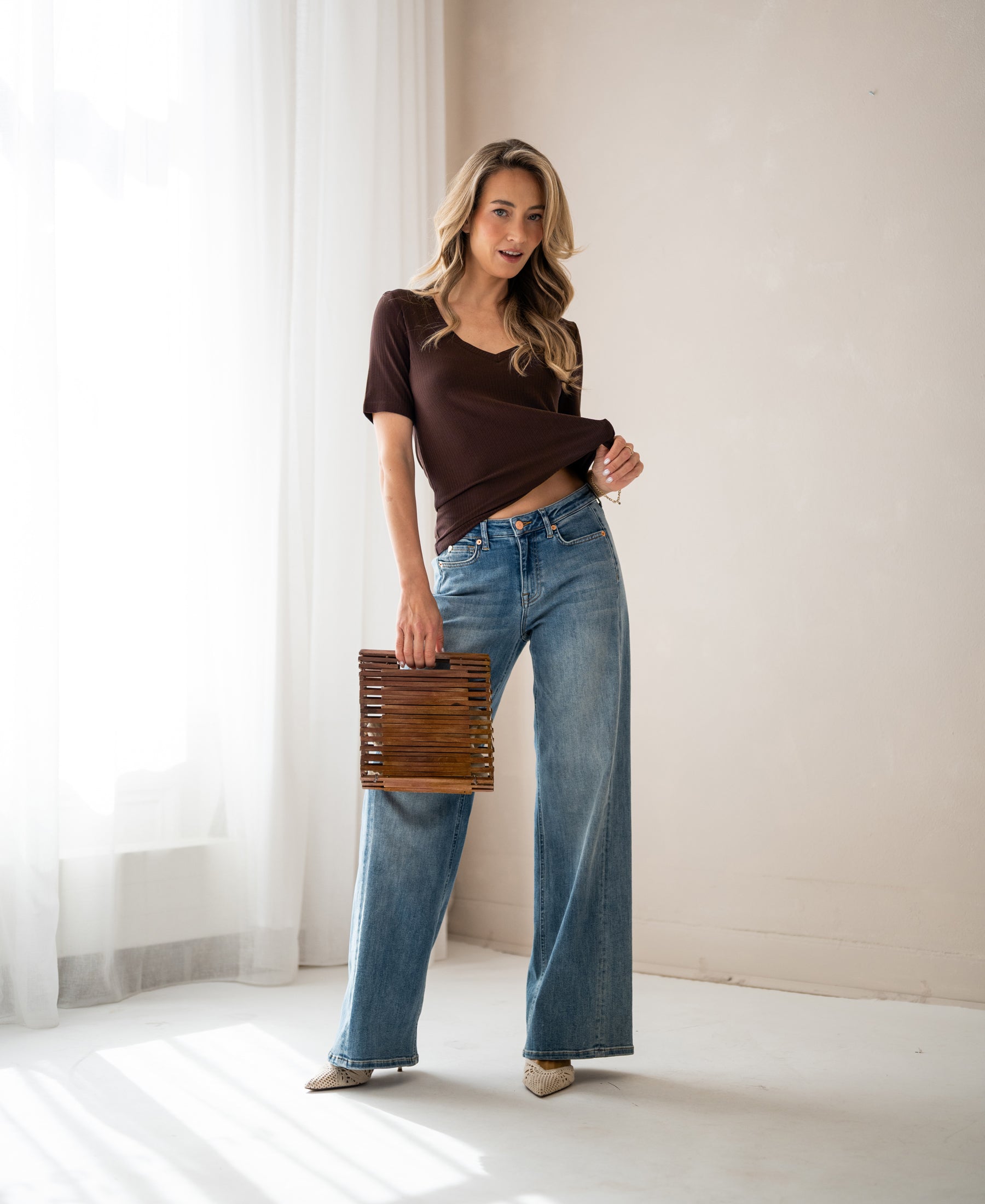 Woman wears the PLEIN PUBLIQUE bamboo T-shirt LES VERSAILLES in chocolate color in a bright room.