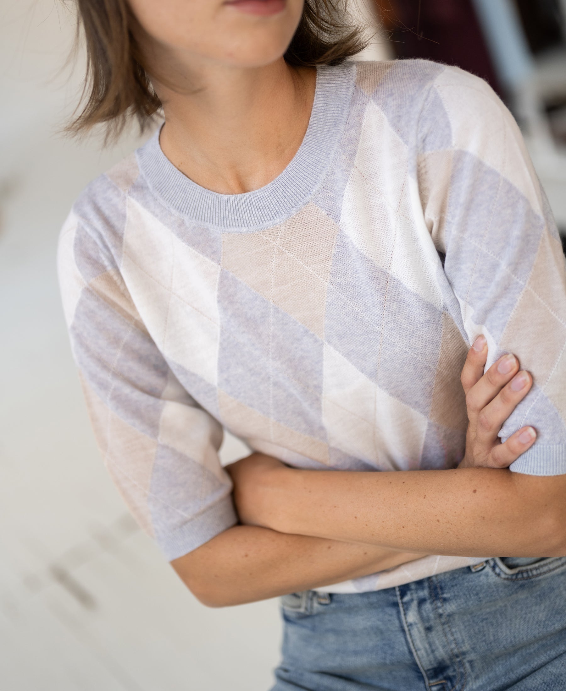 Light grey melange argyle merino wool sweater with short sleeves, shown worn by a woman, arms crossed.