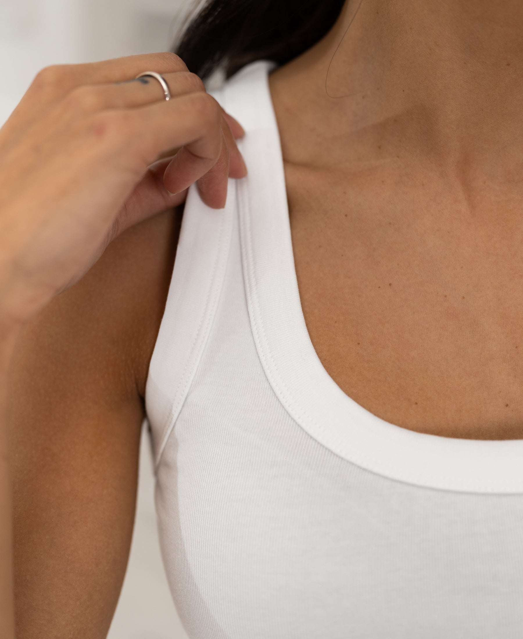 Person adjusts strap on white LA TOULON Luxe & Soft Top, revealing neck and collarbone.