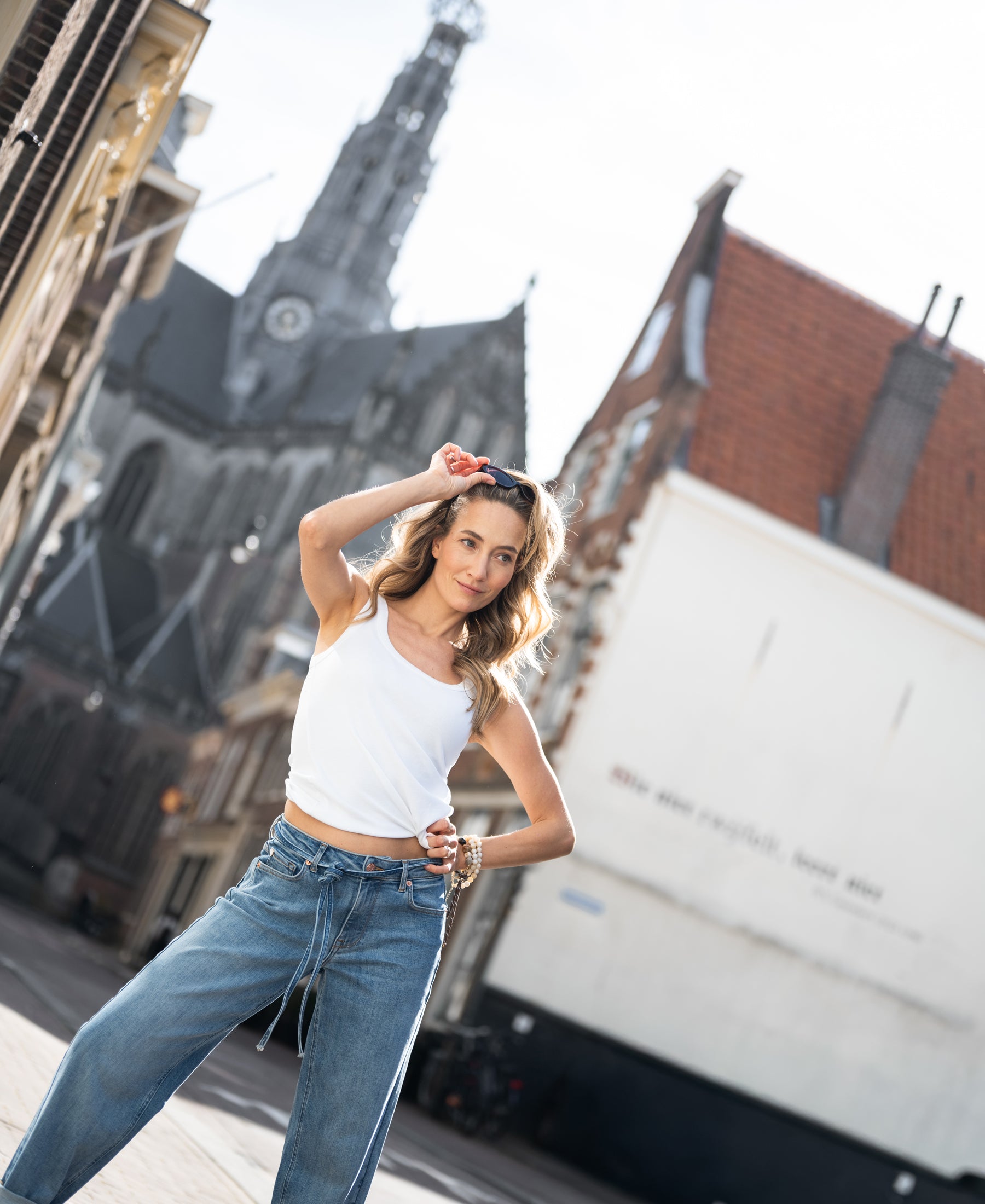 Woman wearing the Luxe & Soft White Top by PLEIN PUBLIQUE, shown standing on a city street.
