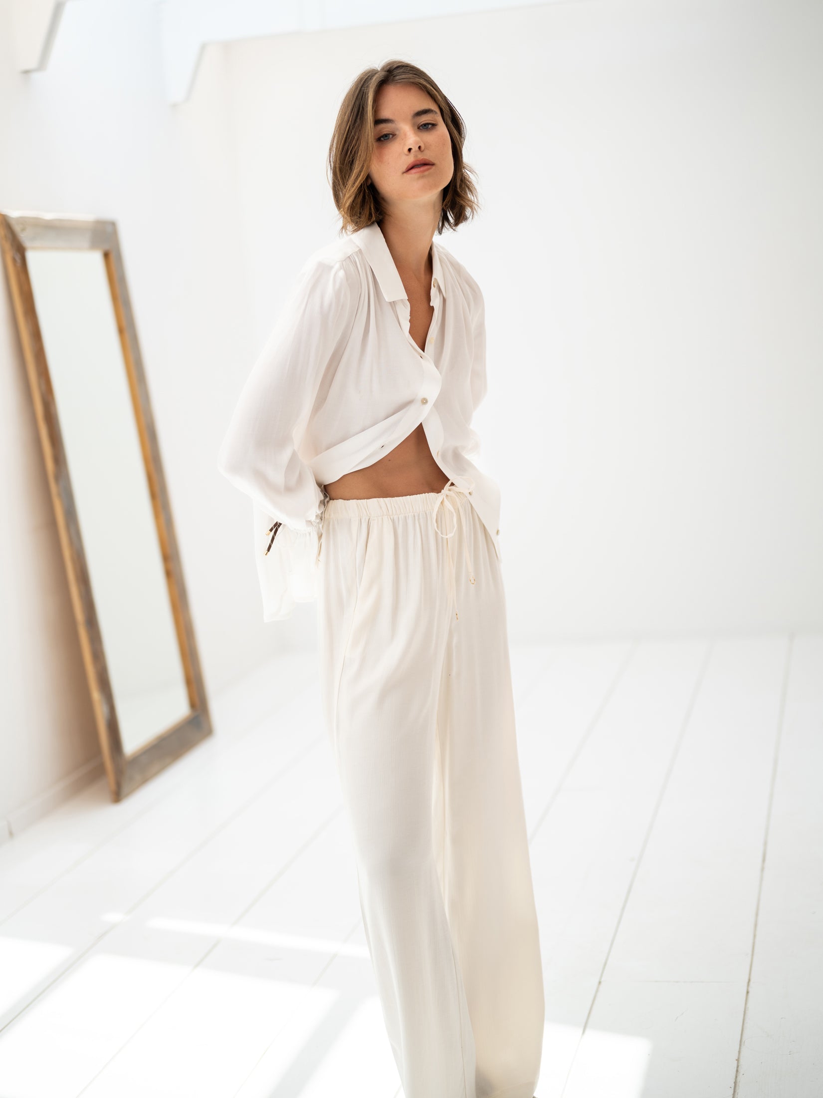 White LA TROYES blouse by PLEIN PUBLIQUE shown in a bright, minimalist room with a mirror.