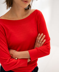 Coral red Tencel-silk boat neck sweater, arms crossed, shown in a bright room.