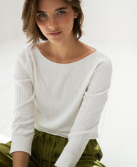 Woman wearing a white PLEIN PUBLIQUE Tencel-silk boat neck sweater, shown in natural light.