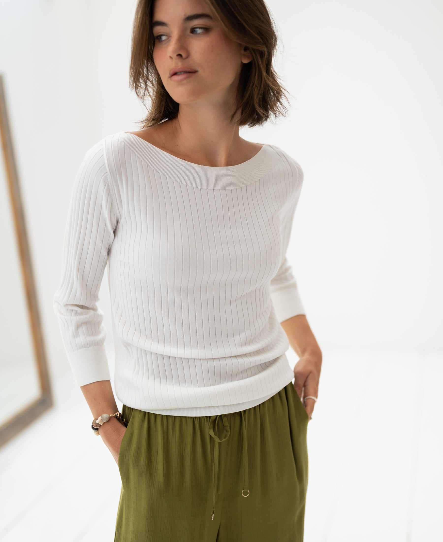 Woman wearing a white Tencel-silk boat neck sweater in a bright, minimalist room.