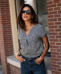 Charcoal dot print Stippen top by PLEIN PUBLIQUE shown from the front against a brick wall.