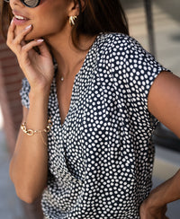 Woman wearing charcoal and ivory polka dot long-sleeve top, touching her face.
