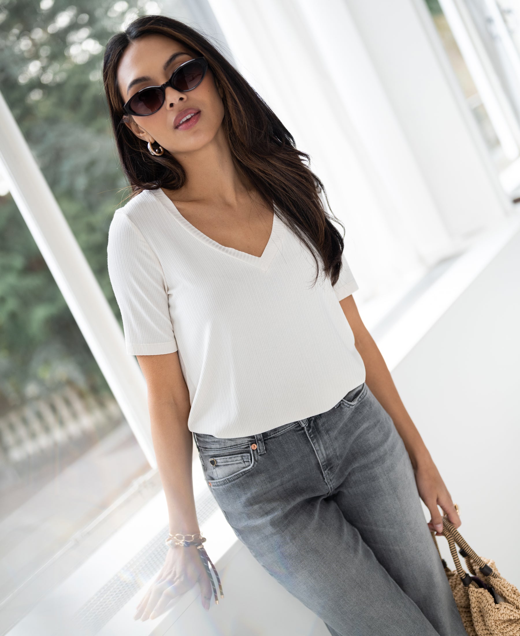Woman wears cream bamboo T-shirt leaning against a window.