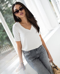 Woman wears cream bamboo T-shirt leaning against a window.