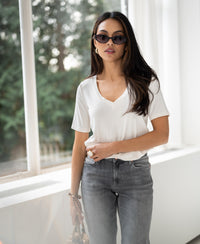 Woman wearing cream PLEIN PUBLIQUE bamboo T-shirt LES VERSAILLES standing by a bright window.
