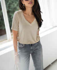 Woman wears light sand bamboo T-shirt by a sunlit indoor window.